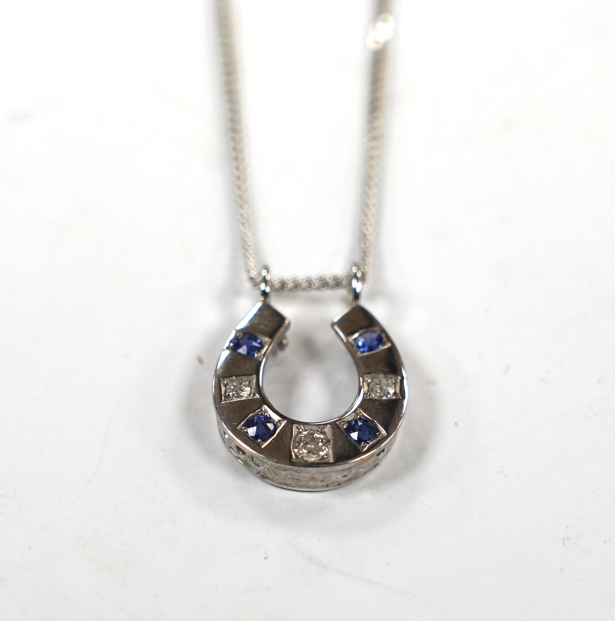 A modern 18ct white gold, sapphire and diamond set horseshoe pendant on chain, overall 44cm, gross weight 5.5 grams. Condition - fair
